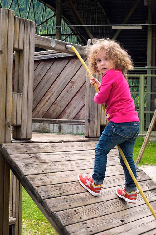 一个小女孩在后院的木制玩具上玩，拿着绳子爬上斜坡。