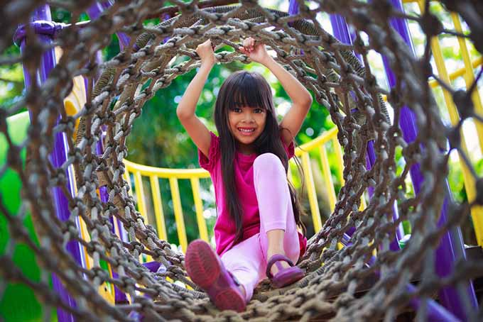 在一个阳光明媚的日子里，一个小女孩在游乐场的绳索隧道里玩耍。