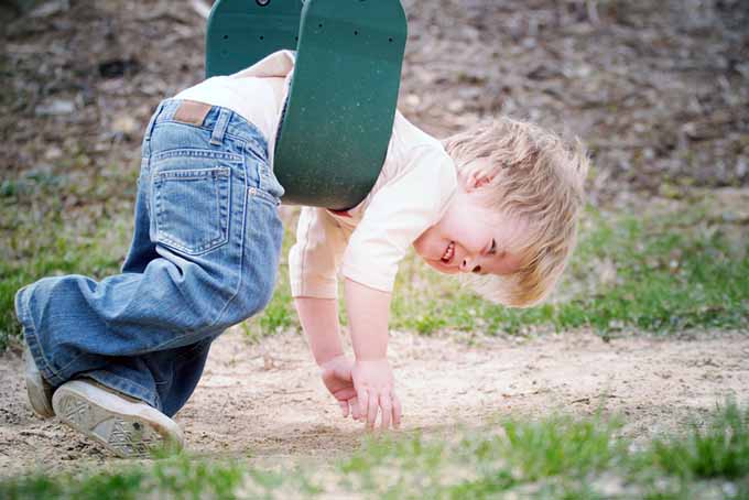 一个小男孩挂在绿色塑料秋千上笑着，背景是沙子和草。