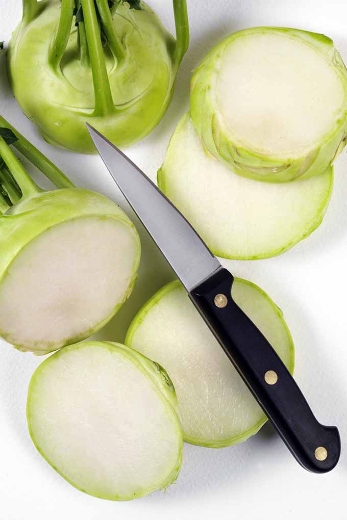 在砧板上切成黄绿色的大头菜，旁边是削皮刀和一整棵直立的大头菜。