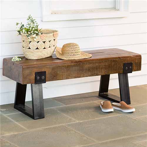 棕色木材和金属回收的木头长凳，上面有一个柳条篮子和帽子，在它前面的瓷砖地板上有一双便鞋。