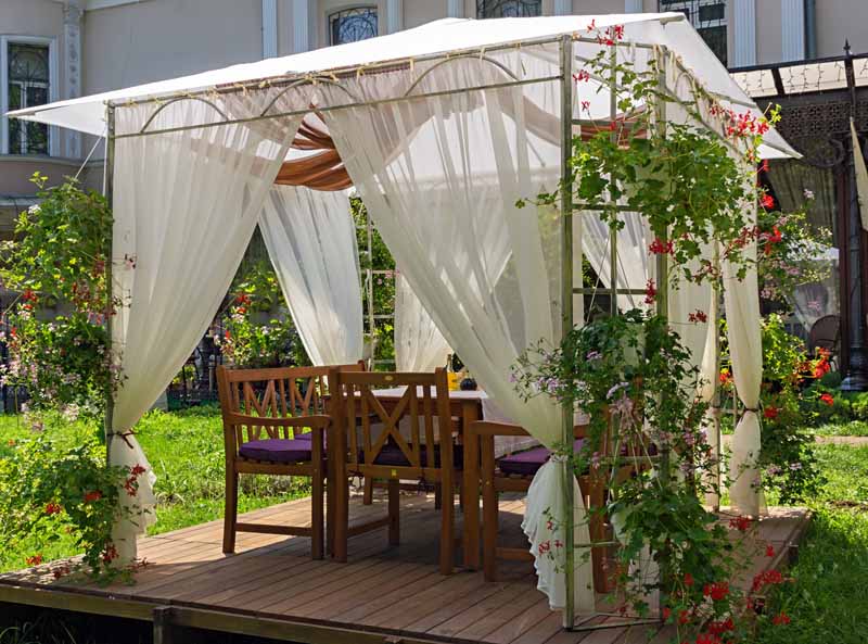 住宅庭院花园中带有织物窗帘的软顶凉亭。