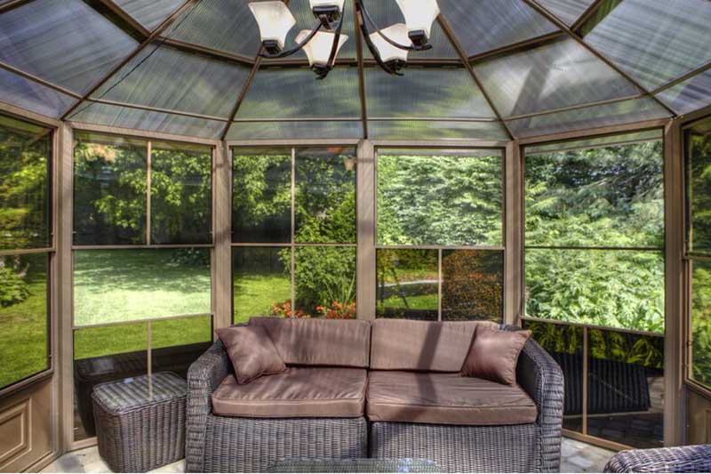 室内景观的花园凉亭网格面板和聚碳酸酯屋顶材料，在一个铝框架。里面有沙发和桌子，透过窗户可以看到花园的景色，