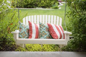 一张白色悬空长椅的特写，俯瞰着夏日花园的场景，背景是草坪和灌木。