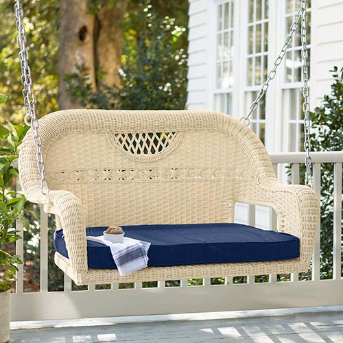圆形边缘的柳条悬椅和甲板上的深蓝色靠垫，以房屋和花园场景为背景的柔焦。