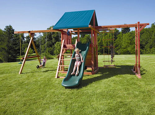 红木大秋千架安装在一个大花园的草坪上，孩子们在阳光明媚的日子里玩耍，背景是蓝天。