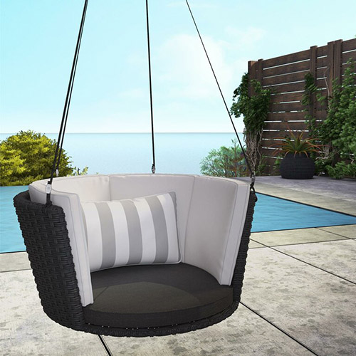 一个圆形的悬椅，由黑色柳条制成，上面有白色条纹靠垫，悬挂在混凝土露台上，露台上有游泳池，背景是大海。