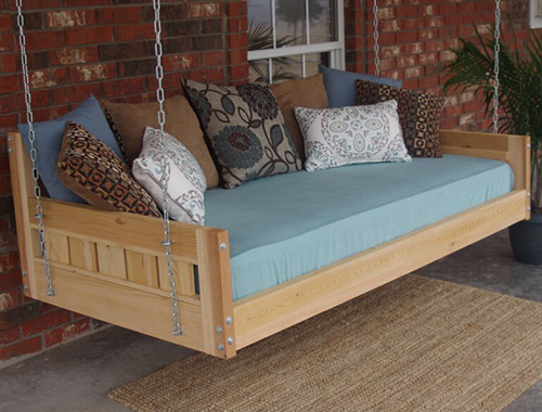 门廊上有一个木制长凳，上面有蓝色的床垫和彩色的靠垫，背景是一座砖房。