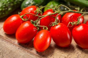 明亮的红色，成熟的“罗马”西红柿，仍然附着在藤蔓上，放置在木质表面上，背景是草本植物。