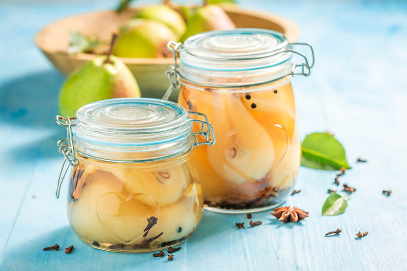 密切的横向图像两个罐子装满了新鲜的梨罐头与成熟水果蓝木表面在一个木制碗背景。