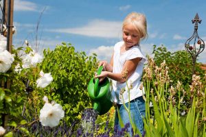 近水平形象的金发的孩子拿着绿色喷壶在花园见蓝天背景。