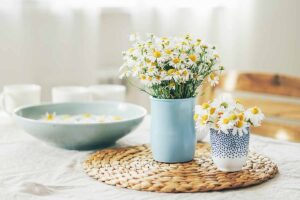 一个水平的图像洋甘菊花在花瓶和碗设置在柳条桌垫。