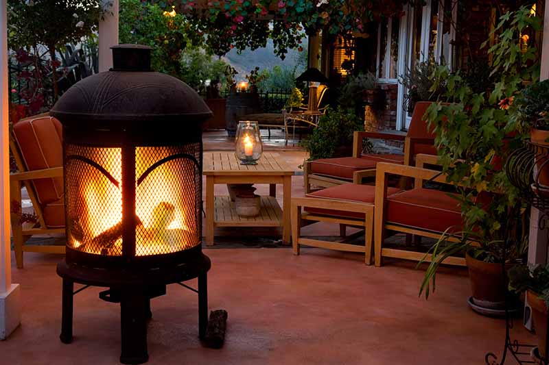 一个水平的户外生活空间的图像，有木制家具，蜡烛和一个燃烧木头的大露台加热器。